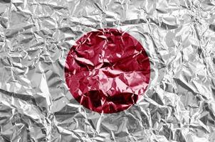 bandeira do japão retratada em cores de tinta em folha de alumínio amassada brilhante closeup. banner texturizado em fundo áspero foto