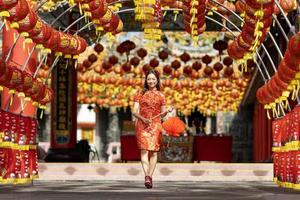 mulher asiática em vestido vermelho cheongsam qipao segurando lanterna enquanto visitava o templo budista chinês durante o ano novo lunar para o conceito de cultura tradicional foto