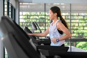jovem atleta asiática feliz corre na esteira, máquina de corrida, no ginásio indoor fitness para a saúde foto