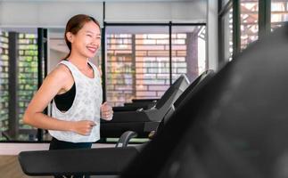 jovem atleta asiática feliz corre na esteira, máquina de corrida, no ginásio indoor fitness para a saúde foto