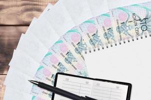 Ventilador e bloco de notas de 100 contas de korun checo com livro de contatos e caneta preta. conceito de planejamento financeiro e estratégia de negócios foto