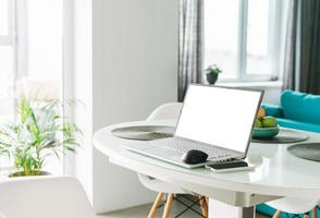 laptop aberto com tela branca na mesa na mesa na sala de estar em casa com interior brilhante, conceito de trabalho remoto foto