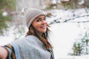 jovem morena linda mulher de chapéu e poncho cinza andando na floresta de inverno foto