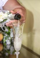 um homem derrama champanhe em um copo elegante. festa de casamento foto