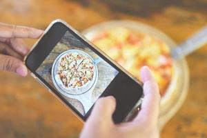 mãos de mulher de fotografia de comida fazem pizza de foto com smartphone - tirando comida de foto para postar e compartilhar em redes sociais com câmera de smartphone em restaurante