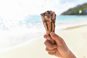 casquinha de sorvete na mão com fundo do mar - sorvete derretendo na praia no verão clima quente oceano paisagem natureza férias ao ar livre, sorvete de chocolate foto