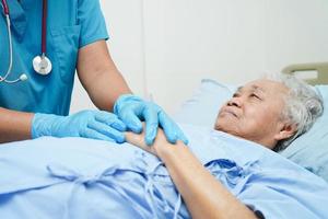 médico de mãos dadas paciente idosa asiática, ajuda e cuidados no hospital. foto