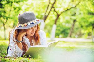 mulher asiática viajar natureza. viajar relaxar. dormir lendo livro no gramado do parque. no verão. foto
