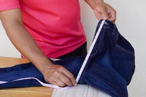 alfaiate closeup usa fita métrica para medir o comprimento da virilha de jeans. conceito, diy, costura. feito â mão. design, conserto ou reparo de corte de roupas. foto