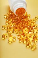 cápsulas de óleo de peixe ômega-3 douradas derramadas de uma jarra em um fundo amarelo foto