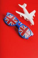 avião branco e óculos de sol com a bandeira do reino unido sobre um fundo vermelho. viajar para a inglaterra. foto