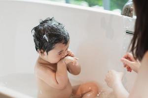 criança bonita asiática tomando banho lavando cabelo limpando banheira de banho com a mãe dela. mãe, amor e cuidado, bebê feliz, inocente, divirta-se brincando com a água, desfrutando. conceito de bebê. foto