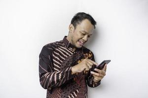 um retrato de um homem asiático feliz vestindo camisa batik e segurando seu telefone, isolado por fundo branco foto