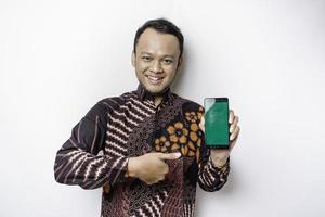 um retrato de um homem asiático sorridente vestindo uma camisa batik e mostrando a tela verde em seu telefone, isolado por fundo branco foto