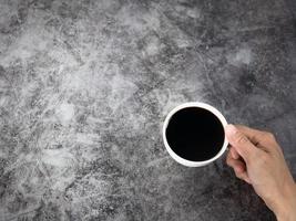 mão segurando a xícara de café preta vista superior escura copie o espaço foto