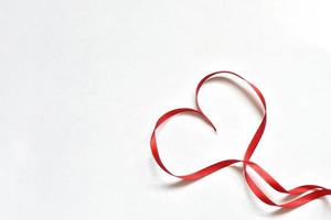 coração feito de fita de cetim vermelha fina disposta sobre um fundo branco foto