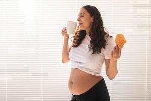 mulher grávida feliz com pães de croissant em casa. gravidez, alimentação e conceito de pessoas foto