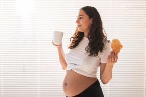 mulher grávida feliz com pães de croissant em casa. gravidez, alimentação e conceito de pessoas foto