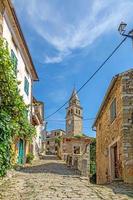 vista sobre a estrada histórica de paralelepípedos para motovun com igreja evangélica durante o dia foto