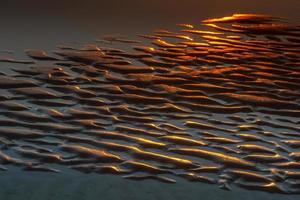 padrões na areia do mar ao pôr do sol foto