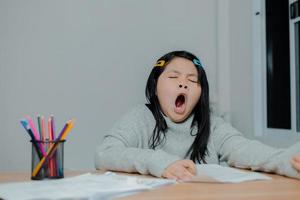 menina asiática bocejando enquanto trabalhava em uma mesa foto