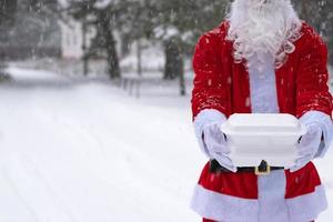 recipientes de serviço de entrega de comida nas mãos do papai noel ao ar livre na neve. promoção de véspera de natal. pedido quente pronto, caixa plástica descartável. catering de férias de ano novo. copie o espaço, simular foto