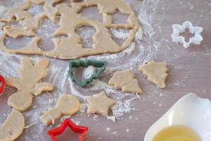 as mãos da mãe e da filha cortaram biscoitos da massa com moldes sobre um tema de natal na forma de um boneco de neve, uma árvore de natal, estrelas foto