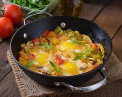 ovos fritos com legumes em uma frigideira em um fundo de madeira foto