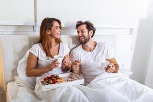 jovem casal apaixonado tomando café da manhã na cama deles. bom Dia. pequeno-almoço saudável na cama. jovem lindo casal apaixonado está tomando café da manhã na cama. foto