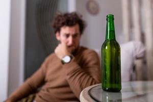 homem alcoólatra pegando uma garrafa de cerveja, homem bebendo sozinho em casa. alcoolismo, dependência de álcool e conceito de pessoas - alcoólatra masculino com garrafa de cerveja bebendo em casa sozinho foto