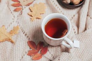 xícara de chá quente, folhas de outono aututmn na manta bege aconchegante. conceito de bebida quente. foto