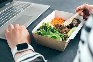 mulher almoçando em tigela reciclada usando laptop. entrega de comida, quarentena, conceito de comida para viagem foto