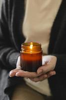 mulher segurando na mão uma vela acesa em uma pequena jarra de vidro âmbar com pavio de madeira. zen e relaxe o conceito.