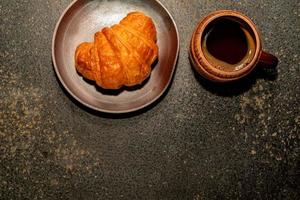 croissant de café da manhã no prato e café na mesa de pedra. foto