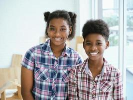 dois irmãos e irmãs afro-americanos abraçam o pescoço e olham o sorriso da câmera. irmã mais velha abraça irmão mais novo pelo pescoço foto