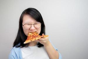 jovem asiática de óculos feliz come pizza em fundo branco. foto