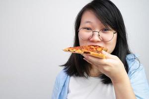 jovem asiática de óculos feliz come pizza em fundo branco. foto
