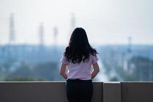 adolescente asiática fica de costas em frente à vista da cidade no telhado do prédio foto
