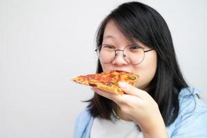 jovem asiática de óculos feliz come pizza em fundo branco. foto