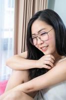 a mulher asiática dos óculos relaxa em sua cama pela manhã em seu quarto. foto