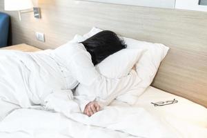 senhora asiática de pijama de camiseta branca de braço comprido deitada de bruços, deitada de bruços na cama com humor e tom experimentados e exaustos. foto