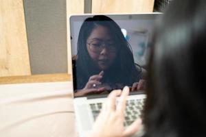 o reflexo da bela mulher asiática da tela do laptop. ela joga laptop e deita na cama em seu quarto. foto