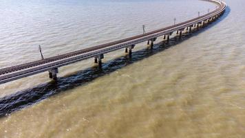 vista aérea de um incrível trem de viagem estacionado em uma ponte ferroviária flutuante sobre a água do lago na represa pa sak jolasid com céu azul em lopburi, tailândia. foto