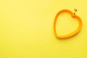 molde de silicone em forma de coração para assar e fritar ovos em um fundo amarelo. vista superior, minimalista, copie o espaço. foto