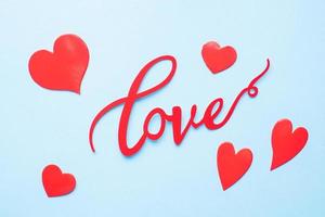 a palavra amor e corações vermelhos sobre um fundo azul, vista superior. cartão de férias para o dia dos namorados. postura plana. foto