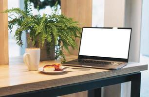 laptop aberto, cheesecakes com geléia, xícara de cappuccino na mesa do café foto