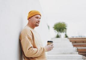 retrato de homem elegante hipster de chapéu amarelo com papel xícara de café na cidade foto