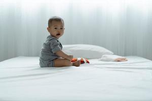 bebê asiático jogando brinquedos e quebra-cabeças de madeira na cama. bebê estão felizes por estarem juntos. atividades para promover o desenvolvimento da idade do bebê. foto