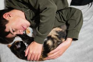 menino adolescente com gatinho deitado no sofá. amor das crianças por animais de estimação. foto