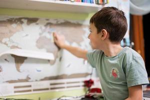 menino mostra a ucrânia com o dedo no mapa-múndi no quarto das crianças. foto